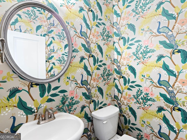 bathroom featuring a sink, toilet, and wallpapered walls