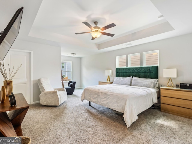 carpeted bedroom with a raised ceiling and ceiling fan