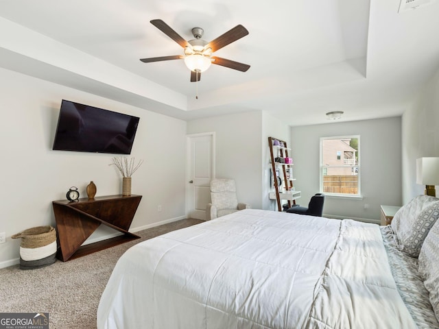 carpeted bedroom with a raised ceiling, baseboards, and a ceiling fan