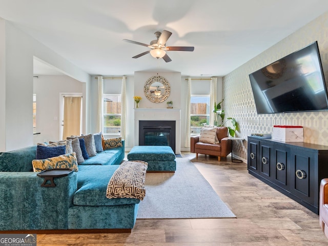 living room with ceiling fan, a glass covered fireplace, and wood finished floors