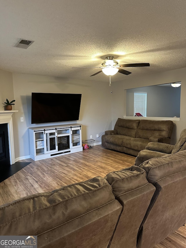 living room with a fireplace, wood finished floors, baseboards, ceiling fan, and a textured ceiling