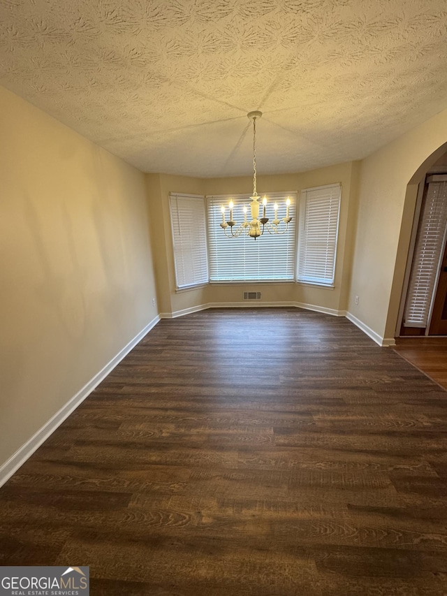 143 Tracy Ln, Mcdonough, GA 30253 - unfurnished dining area with dark wood-type flooring, a chandelier, arched walkways, a textured ceiling, and baseboards