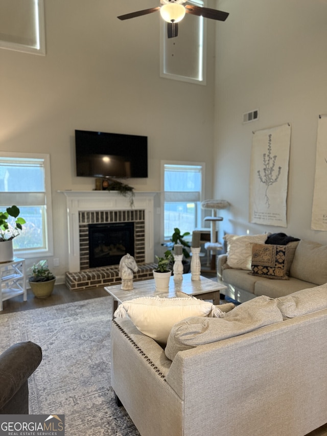 living area with a towering ceiling, a ceiling fan, plenty of natural light, and a brick fireplace