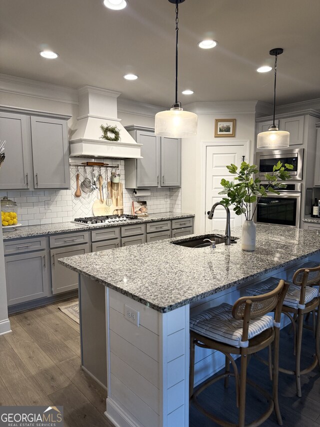 kitchen featuring appliances with stainless steel finishes, premium range hood, gray cabinets, a sink, and crown molding
