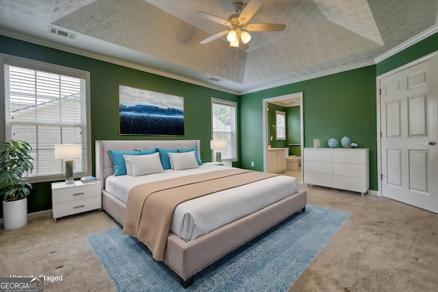 carpeted bedroom featuring a tray ceiling, ornamental molding, connected bathroom, baseboards, and a ceiling fan