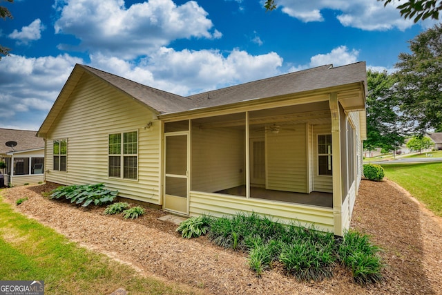 view of side of property featuring a sunroom, a ceiling fan, and a shingled roof