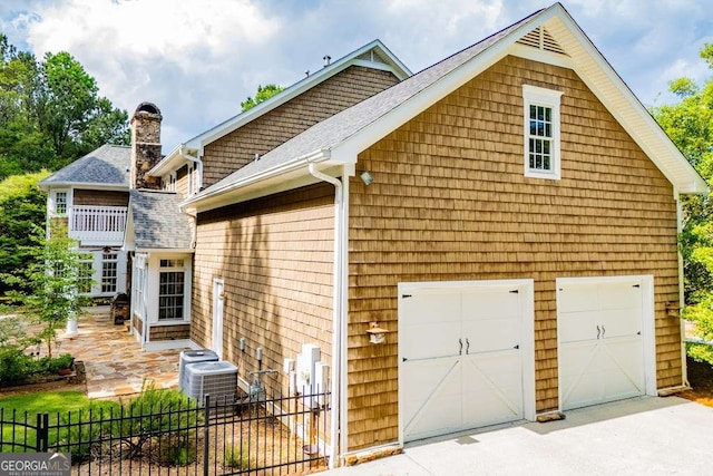 view of home's exterior with a garage, fence, central AC, concrete driveway, and a chimney