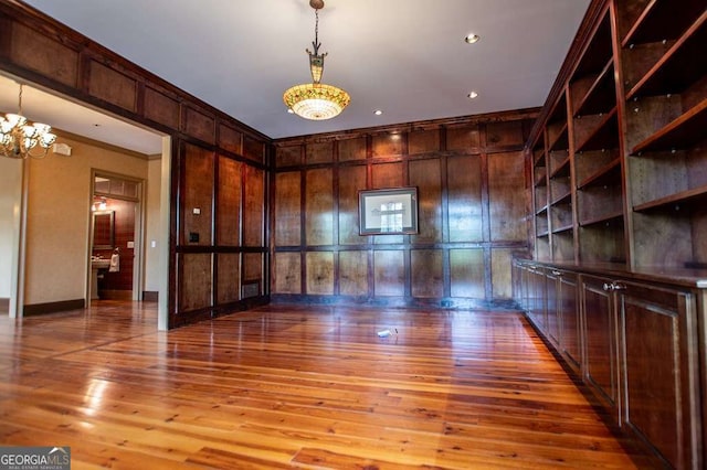 empty room featuring hardwood / wood-style floors, a chandelier, wood walls, ornamental molding, and baseboards