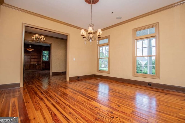 empty room featuring a chandelier, crown molding, wood finished floors, and baseboards