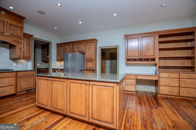 kitchen with freestanding refrigerator, hardwood / wood-style floors, an island with sink, stovetop, and open shelves