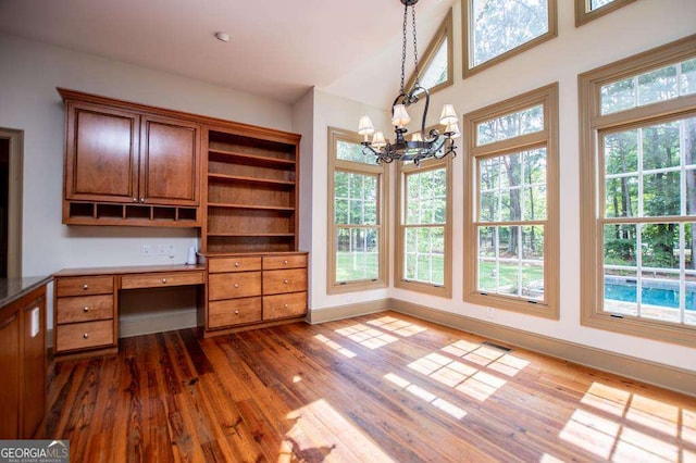 unfurnished office with a chandelier, dark wood-style floors, built in desk, and baseboards