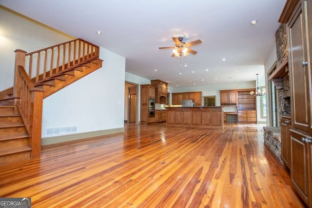 unfurnished living room with ceiling fan, stairway, light wood finished floors, and recessed lighting