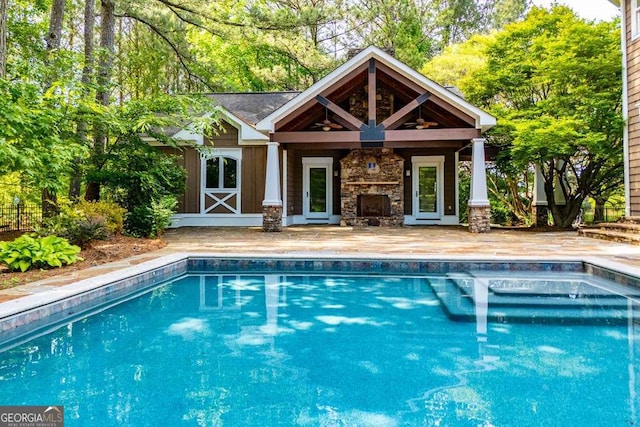 swimming pool featuring an outdoor stone fireplace and a patio