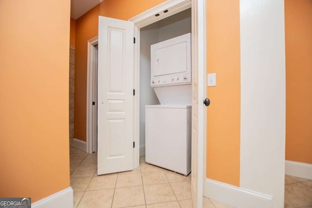 washroom featuring stacked washer / drying machine, light tile patterned floors, and baseboards