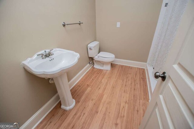bathroom featuring baseboards, wood finished floors, and toilet