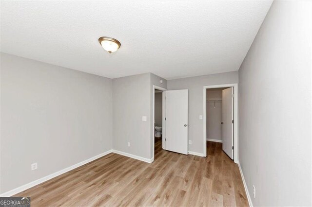 1023 Saint Augustine Pkwy, Locust Grove, GA 30248 - unfurnished bedroom with light wood-style floors, baseboards, a walk in closet, and a closet