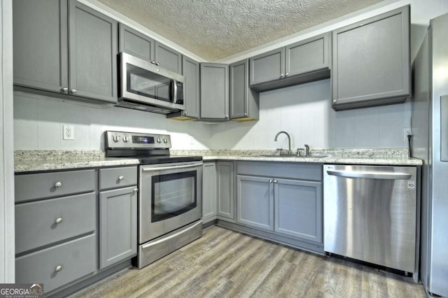 kitchen with appliances with stainless steel finishes, gray cabinets, a sink, light wood finished floors, and a textured ceiling