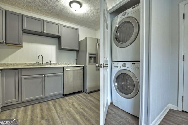 washroom with stacked washing machine and dryer, wood finished floors, a textured ceiling, and baseboards