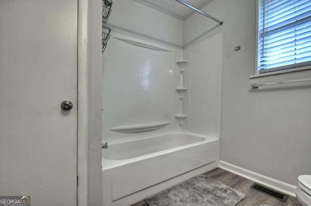 bathroom with wood finished floors, baseboards, toilet, and tub / shower combination