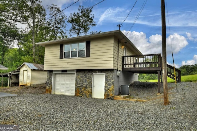 view of side of property with a wooden deck, stone siding, an attached garage, stairway, and a storage shed