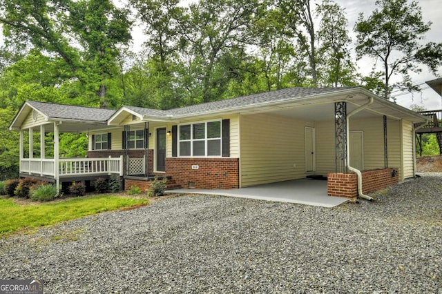 ranch-style house featuring covered porch, gravel driveway, a carport, and brick siding