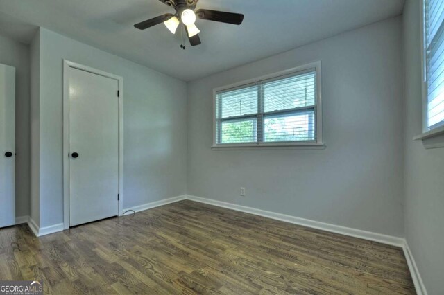 unfurnished bedroom with multiple windows, baseboards, and dark wood-type flooring