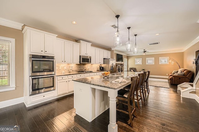 kitchen featuring stainless steel appliances, ornamental molding, open floor plan, a kitchen island with sink, and a kitchen bar