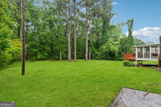 view of green lawn featuring a sunroom and a deck