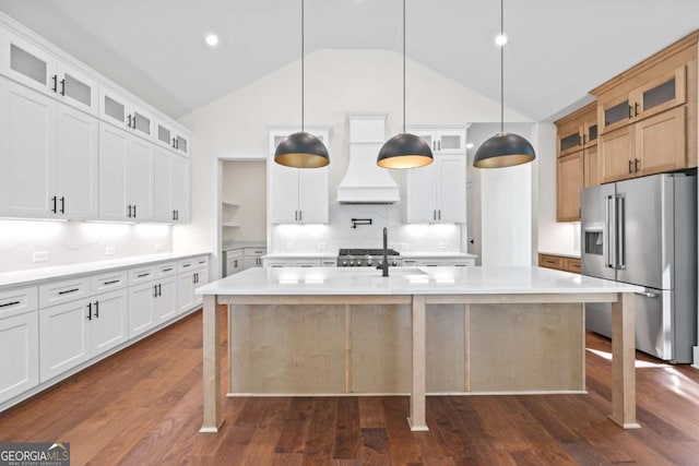 kitchen with high end fridge, custom range hood, light countertops, a center island with sink, and high vaulted ceiling