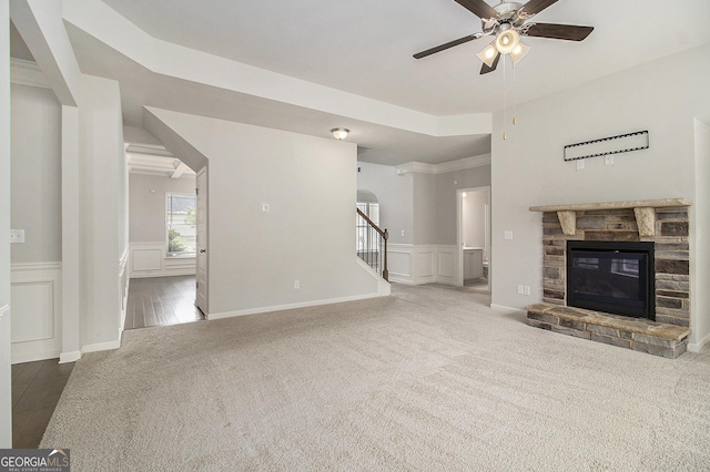 206 Brookview Dr, Newnan, GA 30265 - unfurnished living room featuring a decorative wall, a ceiling fan, carpet, a stone fireplace, and a wainscoted wall