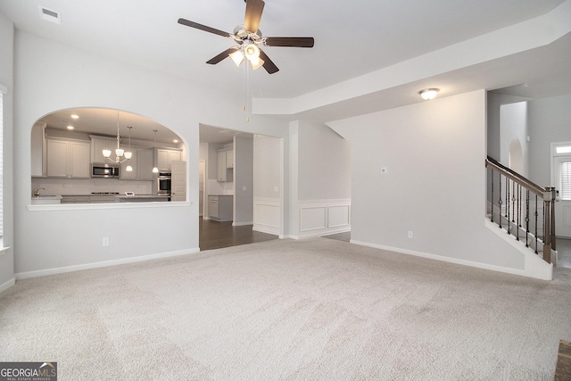 206 Brookview Dr, Newnan, GA 30265 - unfurnished living room with dark carpet, ceiling fan, arched walkways, a chandelier, and stairway