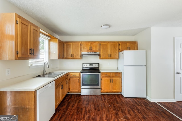 kitchen with white appliances, a sink, under cabinet range hood, dark wood-style floors, and light countertops