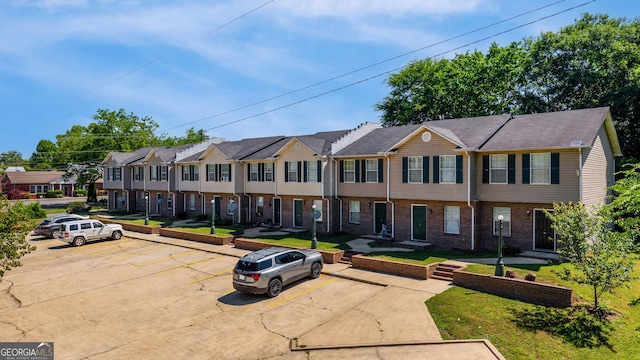 multi unit property featuring a residential view, uncovered parking, brick siding, and a front yard