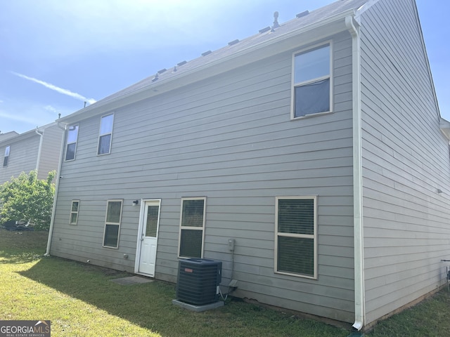rear view of property with central AC unit and a lawn