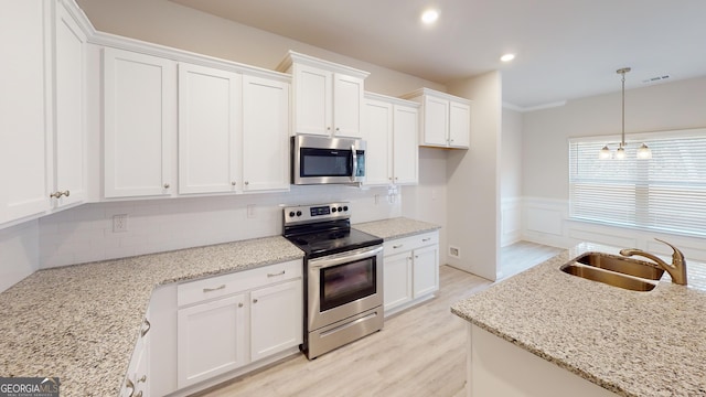 kitchen featuring stainless steel appliances, a sink, white cabinets, light wood-style floors, and light stone counters