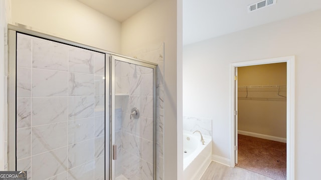 full bath featuring a bath, a stall shower, a walk in closet, and baseboards