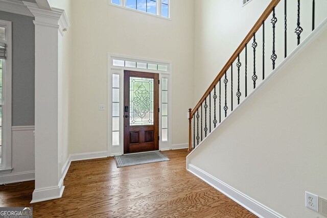 foyer entrance with wood finished floors, ornate columns, stairway, baseboards, and a high ceiling