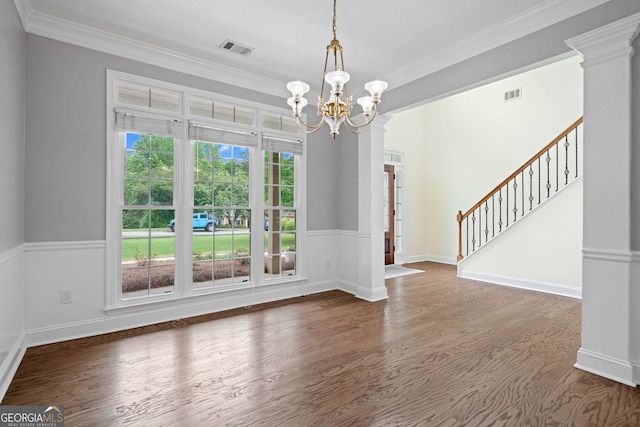 unfurnished dining area featuring a chandelier, wood finished floors, ornamental molding, stairs, and wainscoting