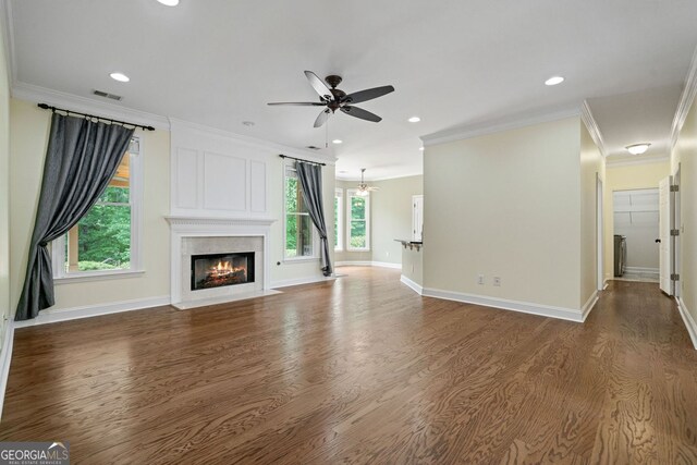 unfurnished living room with a ceiling fan, wood finished floors, a premium fireplace, ornamental molding, and recessed lighting