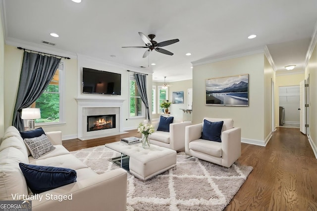 living area with wood finished floors, ceiling fan, crown molding, baseboards, and a fireplace with flush hearth