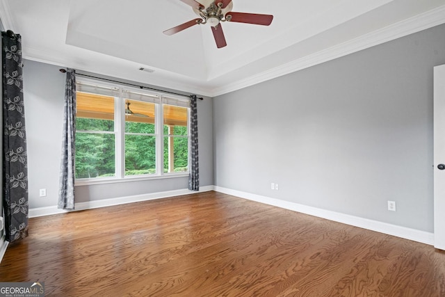 unfurnished room featuring a raised ceiling, ceiling fan, wood finished floors, ornamental molding, and baseboards