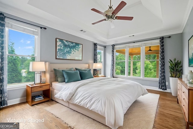 bedroom featuring a raised ceiling, baseboards, light wood-type flooring, ornamental molding, and a ceiling fan