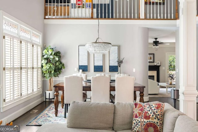 dining room with a towering ceiling, a ceiling fan, baseboards, a chandelier, and wood finished floors