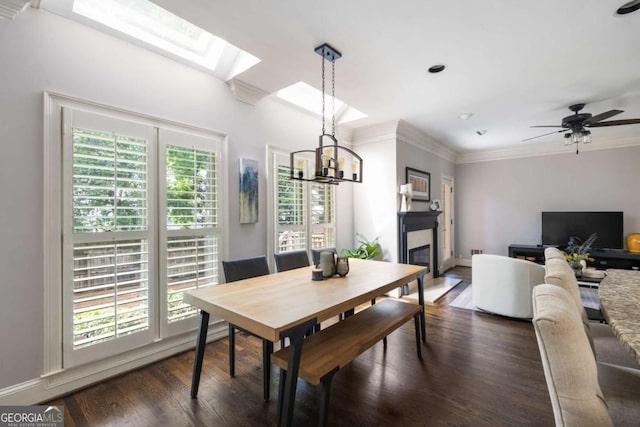 dining space featuring ornamental molding, a skylight, a chandelier, dark wood-style flooring, and a glass covered fireplace