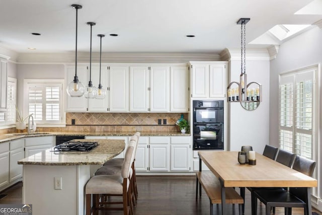 kitchen with a sink, dark wood-type flooring, white cabinets, a chandelier, and a kitchen island