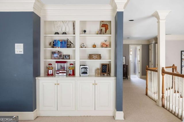 hallway featuring light carpet, baseboards, ornamental molding, decorative columns, and an upstairs landing