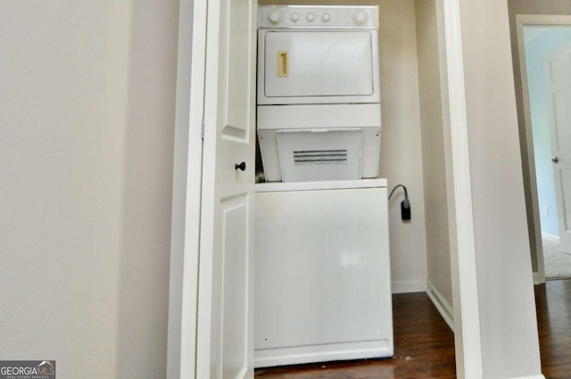 washroom featuring stacked washing machine and dryer, wood finished floors, and baseboards