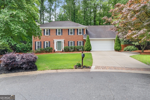 colonial inspired home featuring an attached garage, concrete driveway, a front yard, and brick siding
