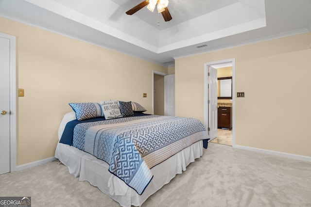 bedroom featuring light carpet, a raised ceiling, baseboards, a ceiling fan, and ensuite bath