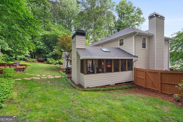 back of property with a chimney, roof with shingles, and a sunroom